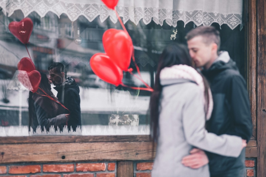 A woman and a man kiss in front of a shopfront.