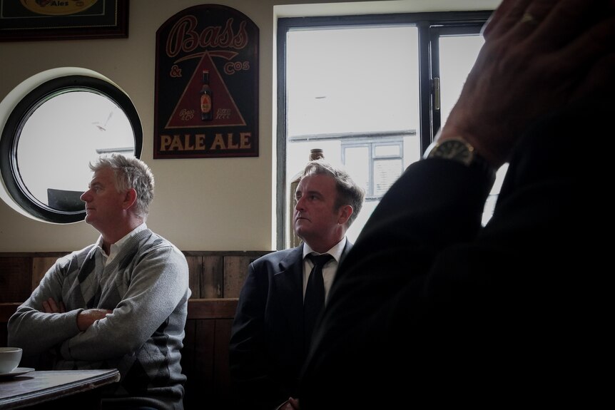 A man looking at a screen off camera in a pub sitting near other diners.