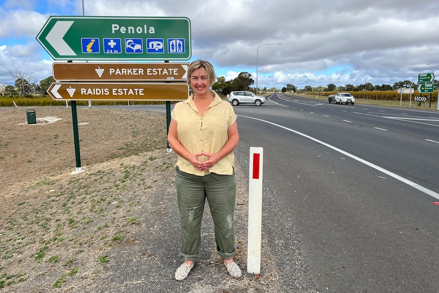 A woman standing next to a road and a sign saying Penola
