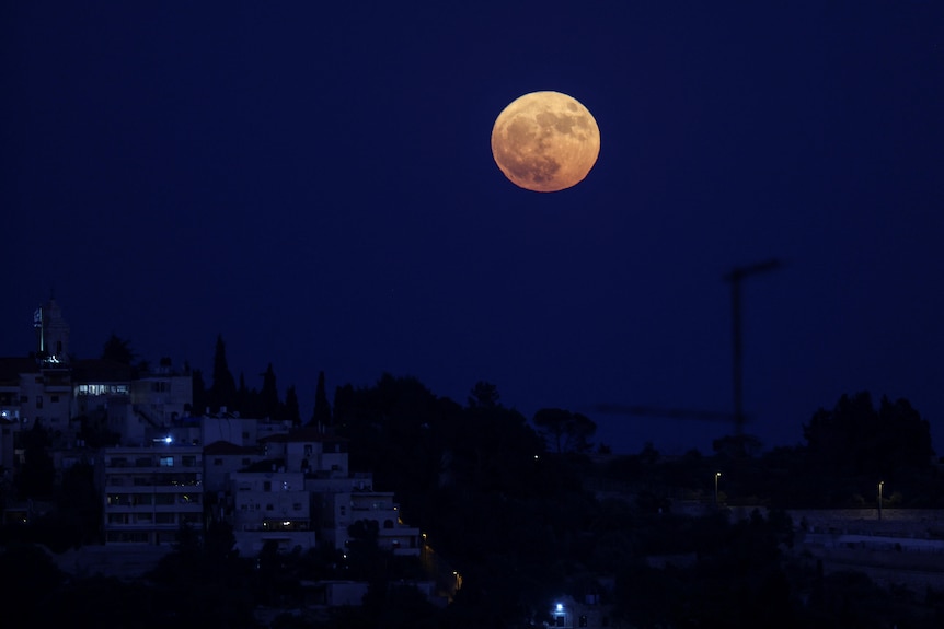 A glowing full moon rises in the night sky 