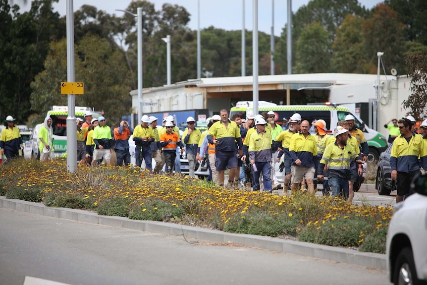 Construction workers in hi-vis clothing and hard hats walk off site at Curtin University after a roof collapse.