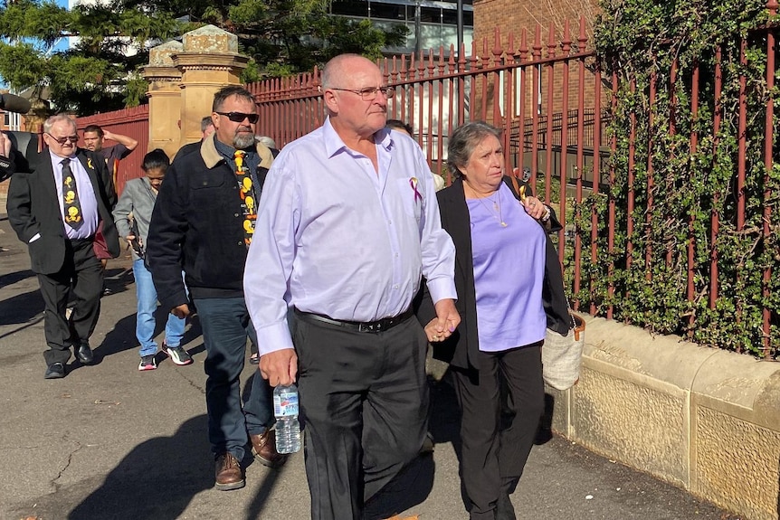 A woman in a purple shirt walking and holding hands with a partner walks toward a court building.