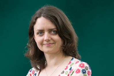 A woman wearing a patterned dress stands with her arms crossed and a slight smile on her face