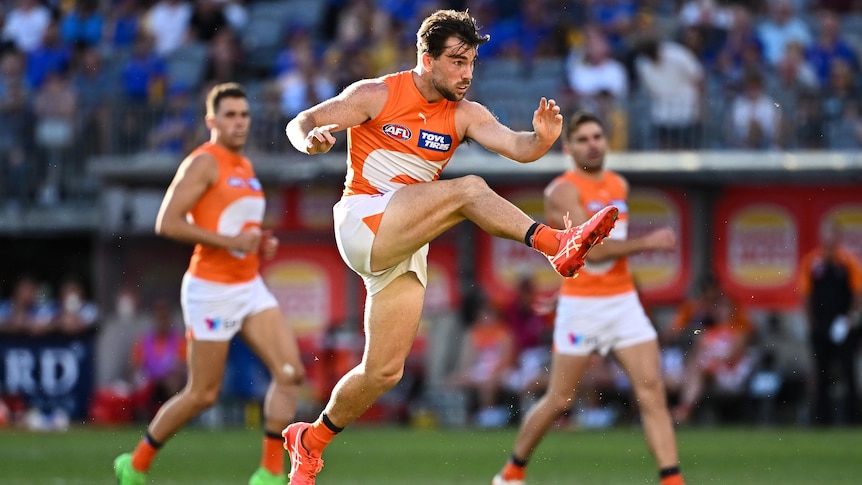 A GWS AFL player is shown with legs extended after a big kick for goal.