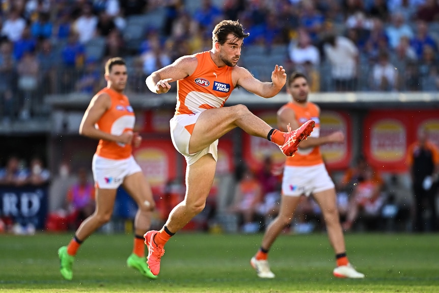 A GWS AFL player is shown with legs extended after a big kick for goal.