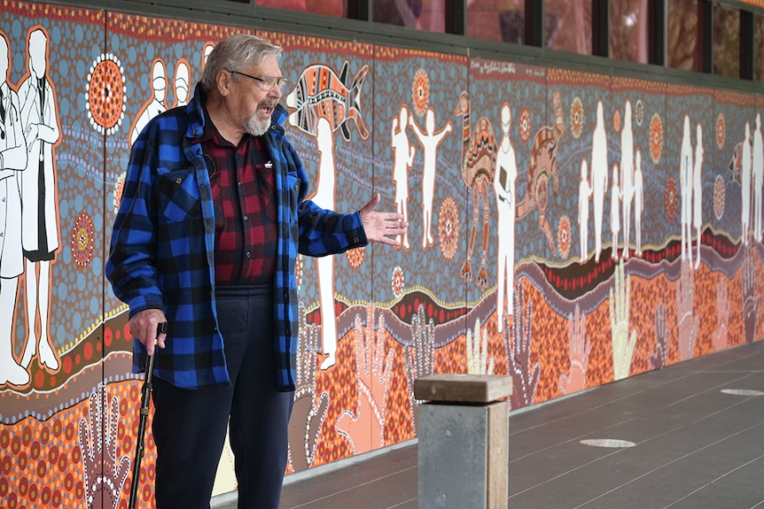 A man in a blue flannel jacket speaking in front of a mural