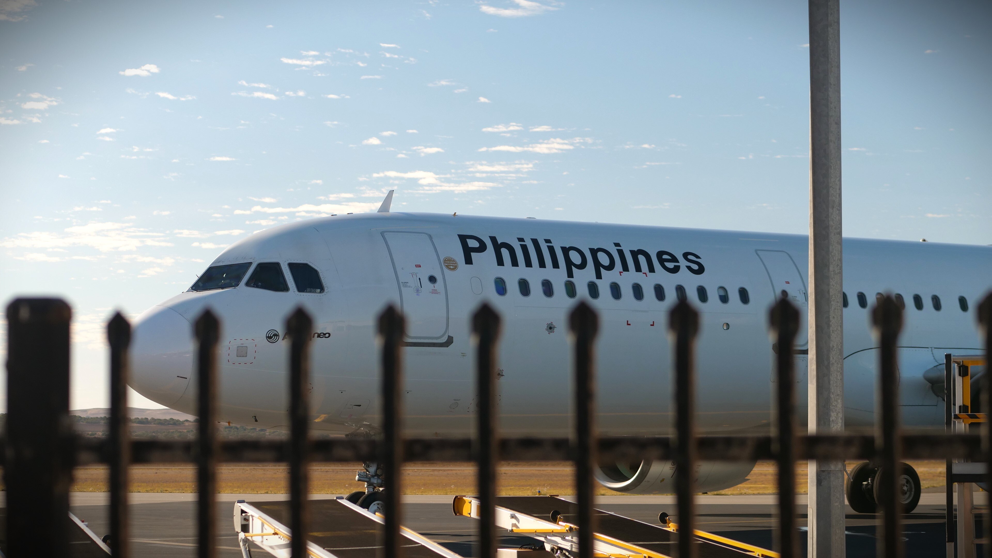 A Phillipines Airlines plane parked on a runway viewed through a black steel fence.