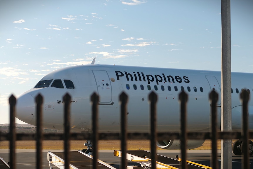 A Phillipines Airlines plane parked on a runway viewed through a black steel fence.