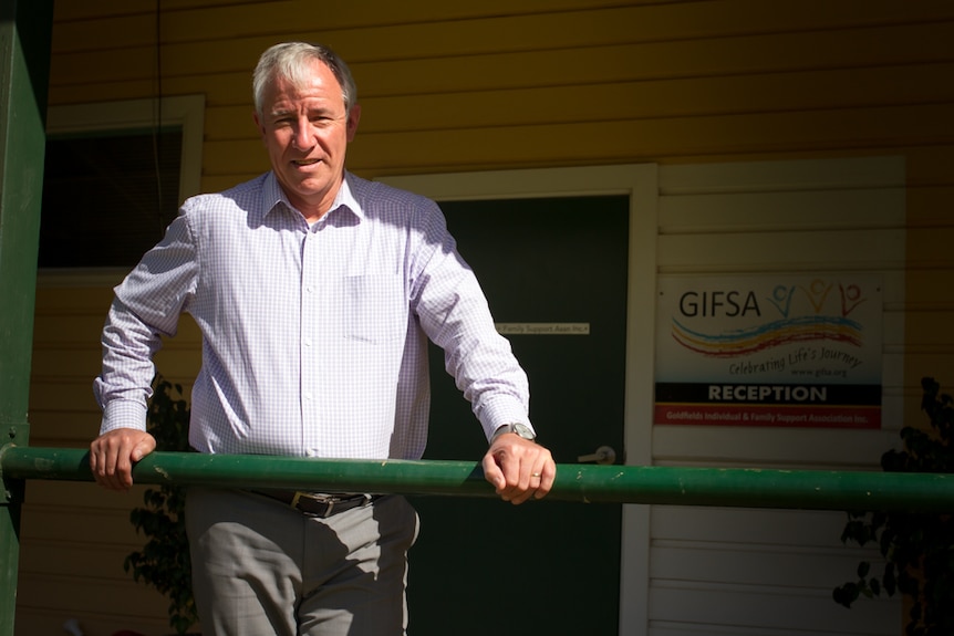 A man leans on a banister out the front of a building with a sign that says GIFSA.