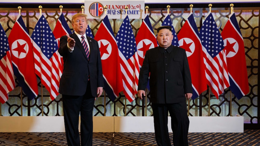 Donald Trump holds out his arm standing next to Kim Jong-un.