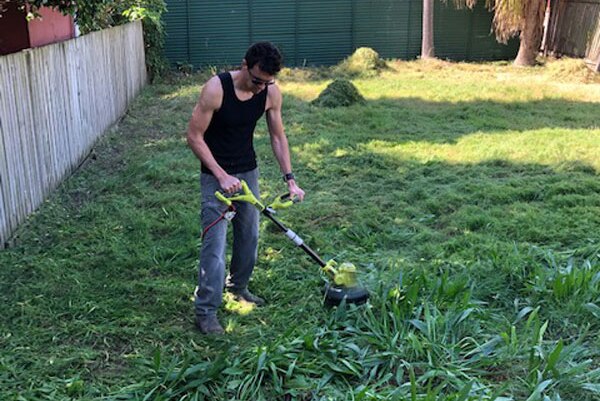 Volunteer Amiel Matthews uses a whipper snipper to tackle the overgrown backyard at Anne O'Connor’s house in Brisbane.