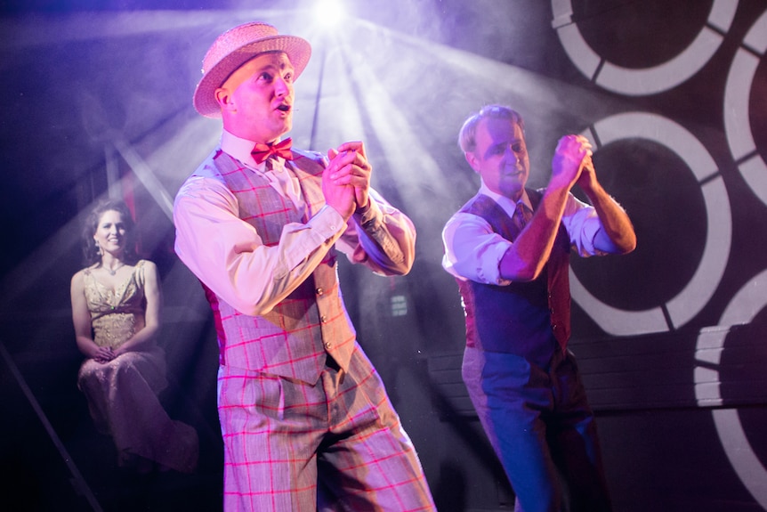 Scene from Evie May featuring two men in a vaudeville double act, as woman in a ballgown watches on.