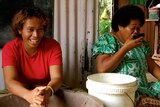 A Fijian woman makes kava while another drinks kava from a bowl.