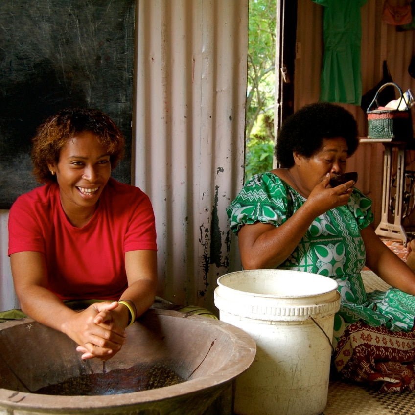 A Fijian woman makes kava while another drinks kava from a bowl.
