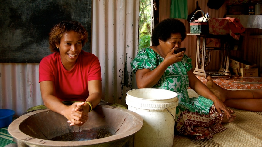 A Fijian woman makes kava while another drinks kava from a bowl.