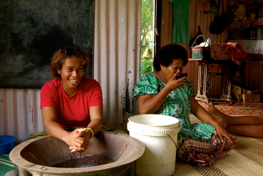 A Fijian woman makes kava while another drinks kava from a bowl.