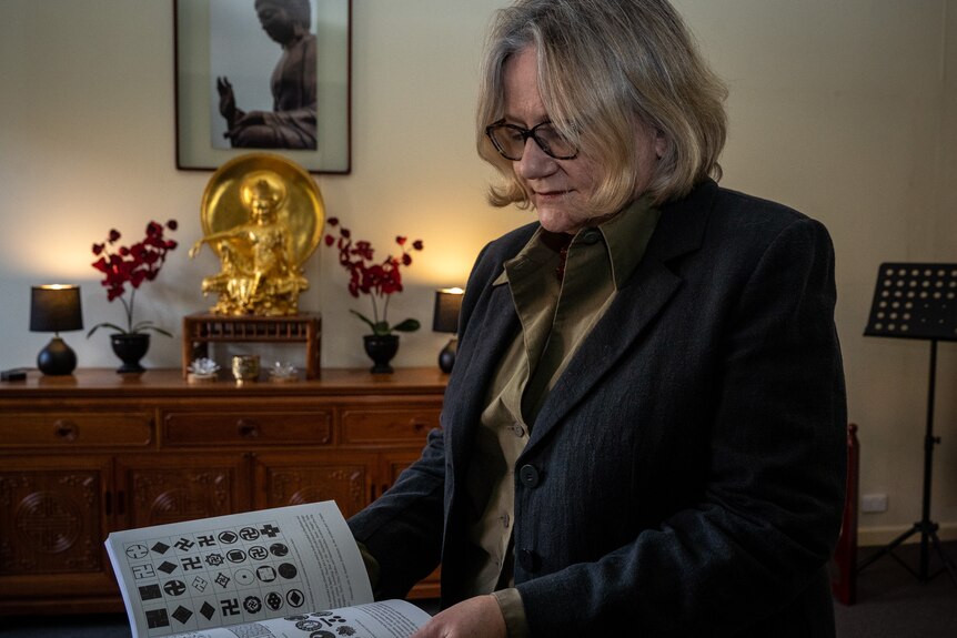 a woman with blonde hair holds a book showing a variety of religious swastika symbols