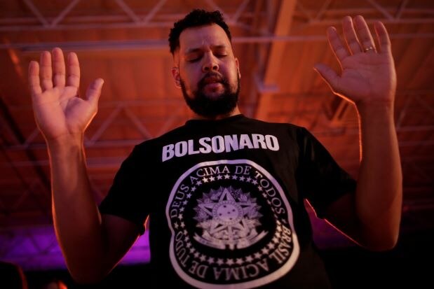 Young Brazilian Evangelical Bolsonaro supporter praying with hands raised