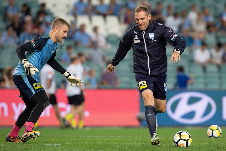 A male goalkeeper wearing blue tries to save a ball during practice