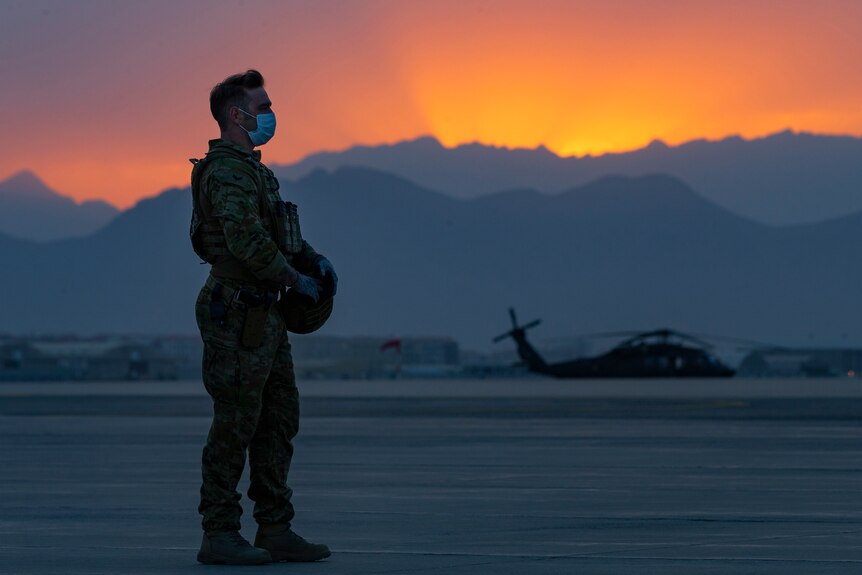 一名戴着口罩的澳大利亚士兵站在停机坪上，太阳在他身后落下