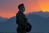 An Australian solider wearing a face mask stands on a tarmac as the sun sets behind him