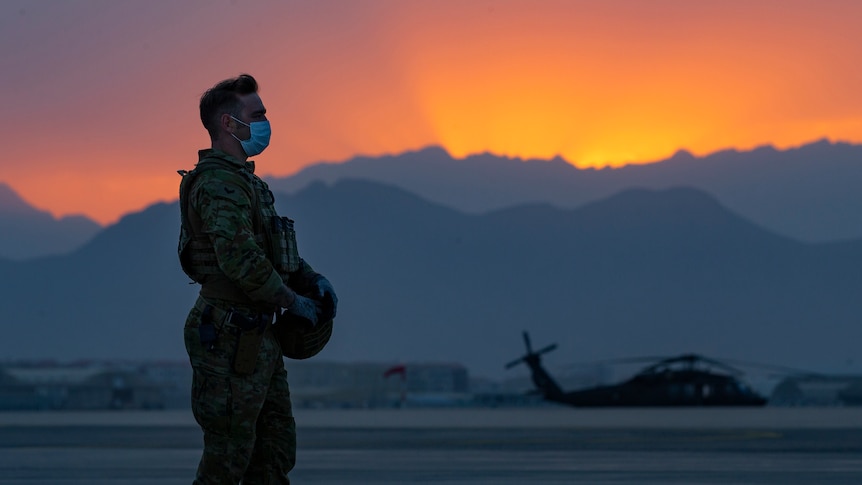 An Australian solider wearing a face mask stands on a tarmac as the sun sets behind him