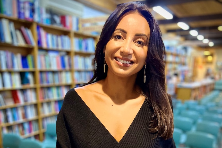 A woman smiling and looking at the camera in a library.