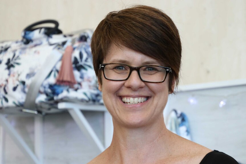 A woman with short hair and wearing glasses stands in front of an art mural