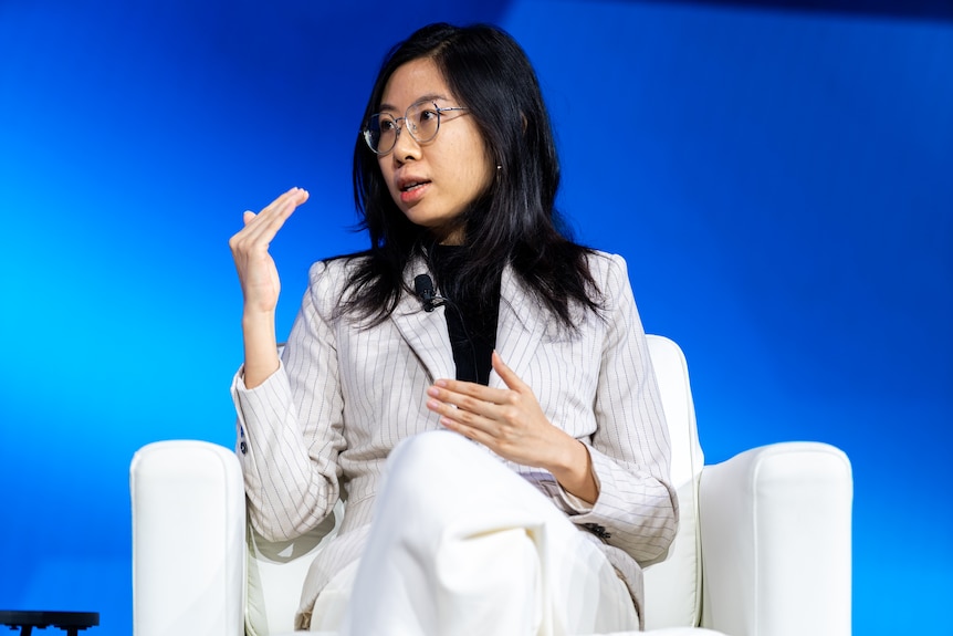 A woman with black hair sits on a stage in a talkback situation