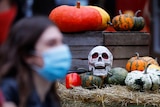 A woman in a disposable face masks walks in front of a fake skull and pumpkins laid out for Halloween.