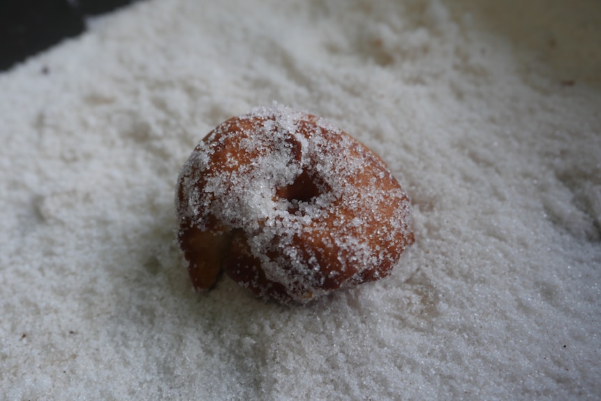 A small, sugar-covered doughnut sits in a pan of sugar