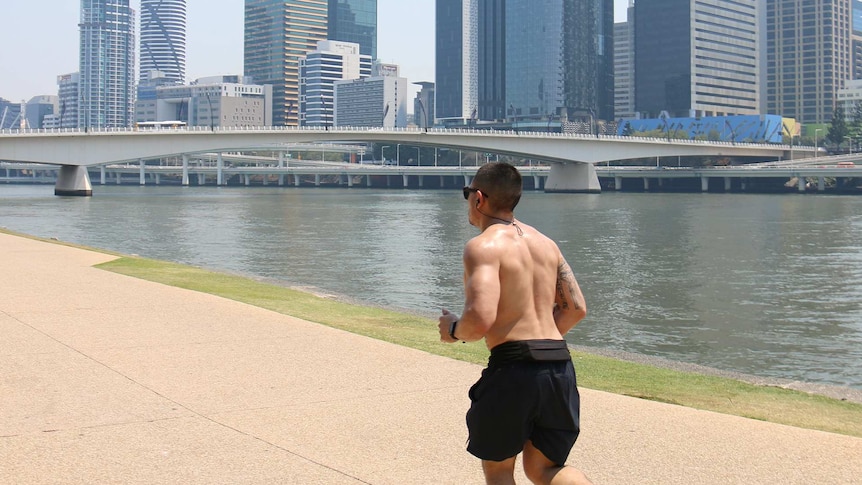 A shirtless man jogs along the Brisbane River, the sky is hazy.