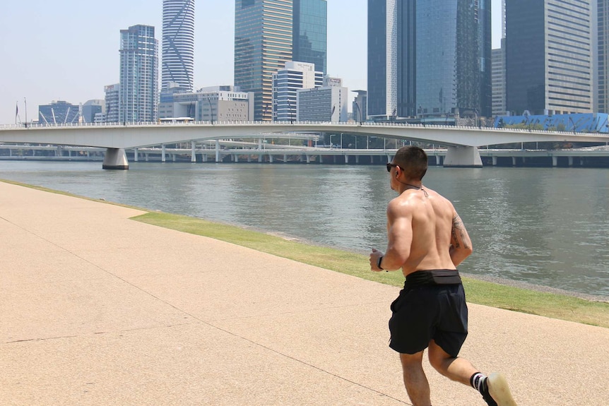 A shirtless man jogs along the Brisbane River, the sky is hazy.