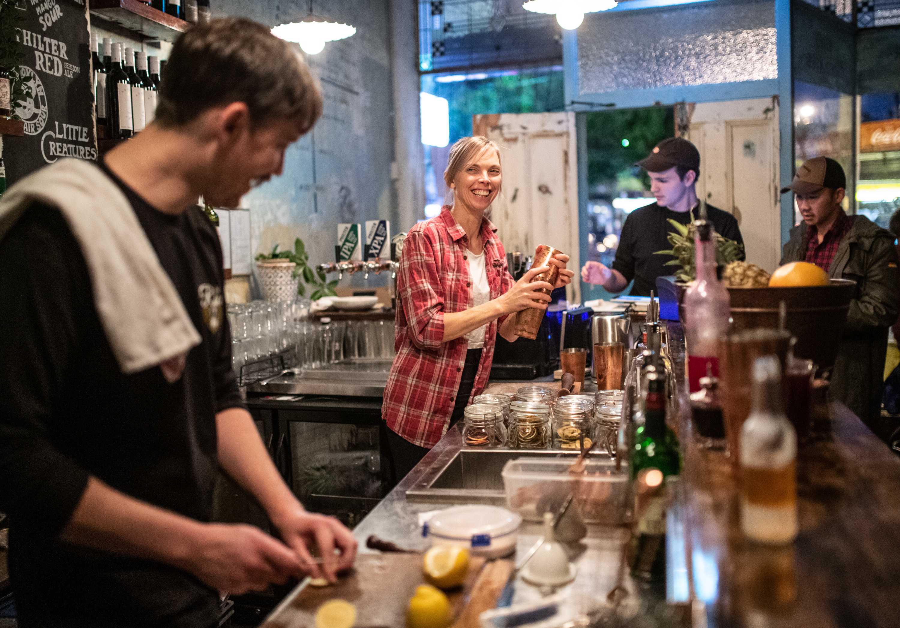 A female bartender smiles at a colleague cutting lemons as she shakes up a cocktail for waiting patrons