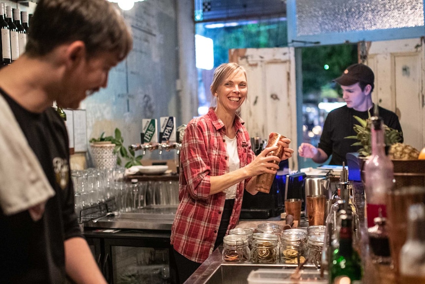 A female bartender smiles at a colleague cutting lemons as she shakes up a cocktail for waiting patrons
