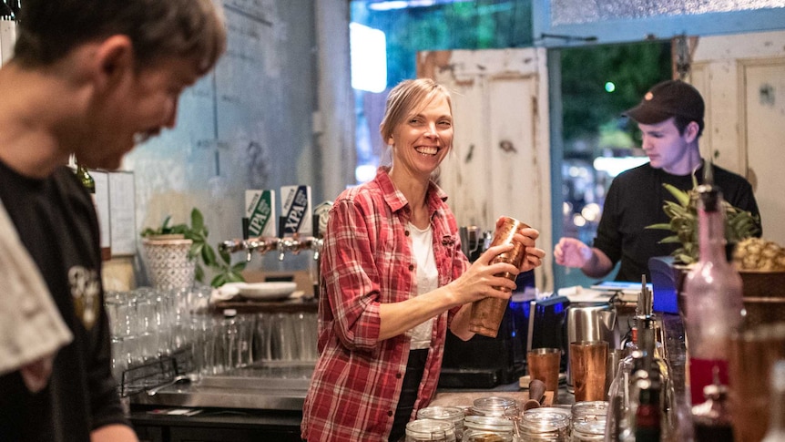 A female bartender smiles at a colleague cutting lemons as she shakes up a cocktail for waiting patrons