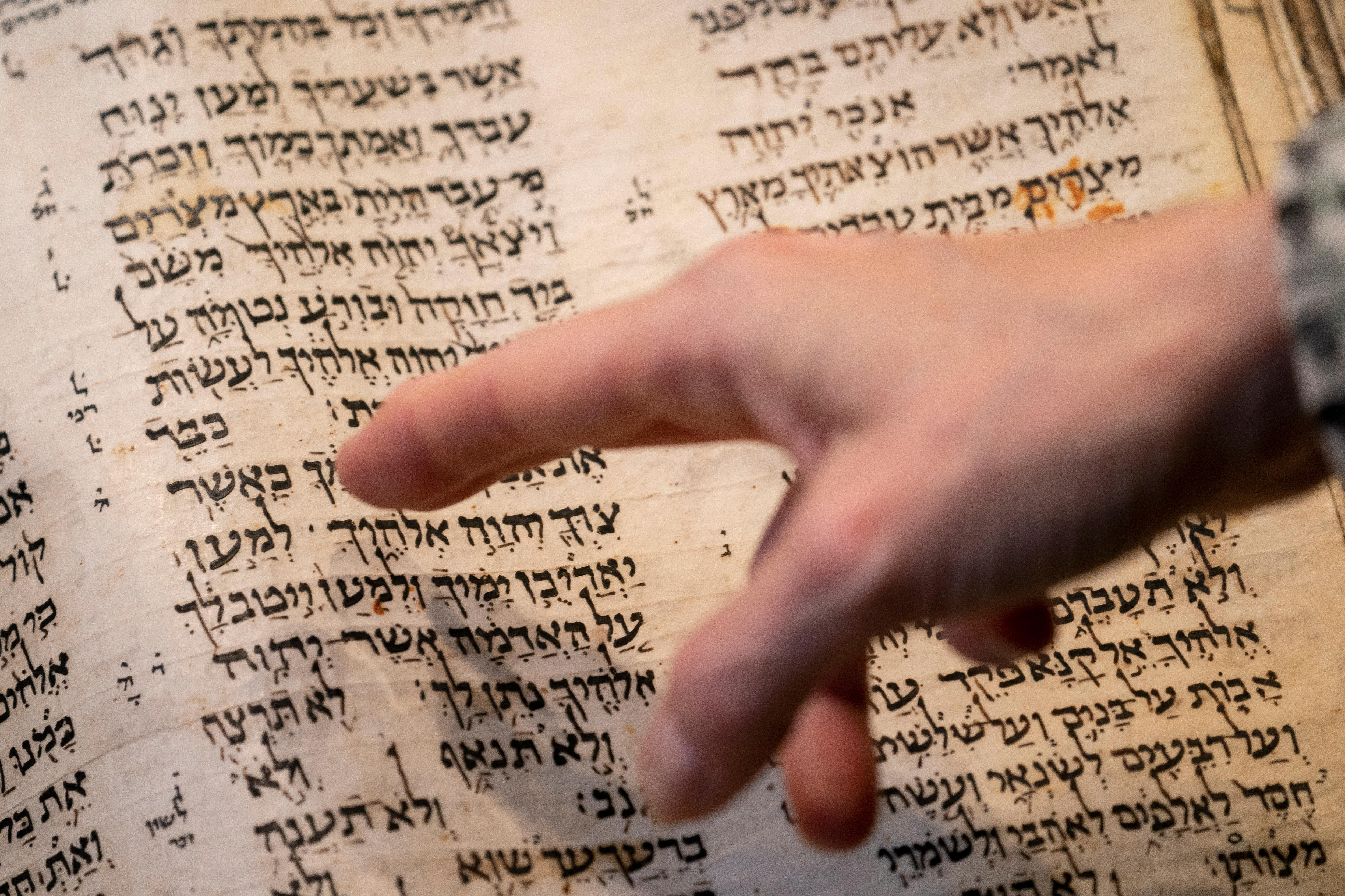 A finger points at the page of an old book which is written in Hebrew.