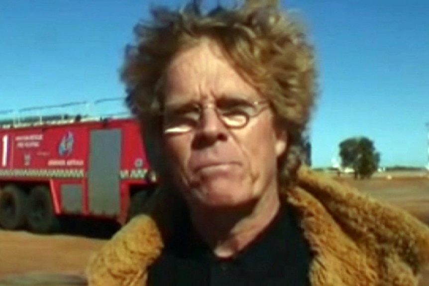 A close-up of face of a man with curly red hair who is standing outside