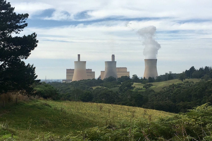 A  large power plant blowing smoke with green rolling hills in the foreground.