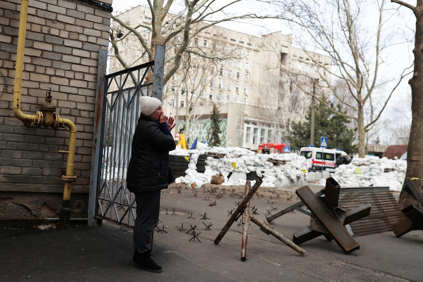 A woman stands outside in Mykolaiv where there are ambulances in the background.
