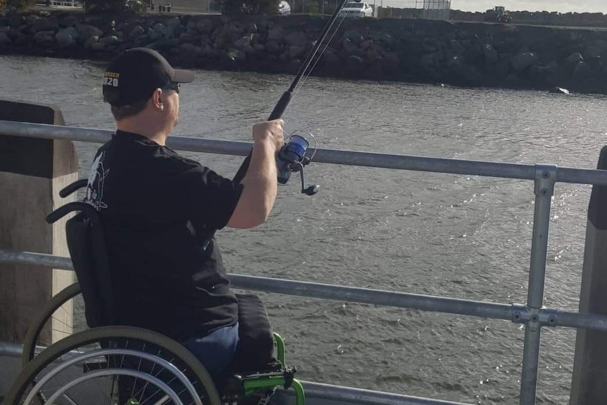 A man in a wheelchair on a jetty with a fishing rod cast out into the water