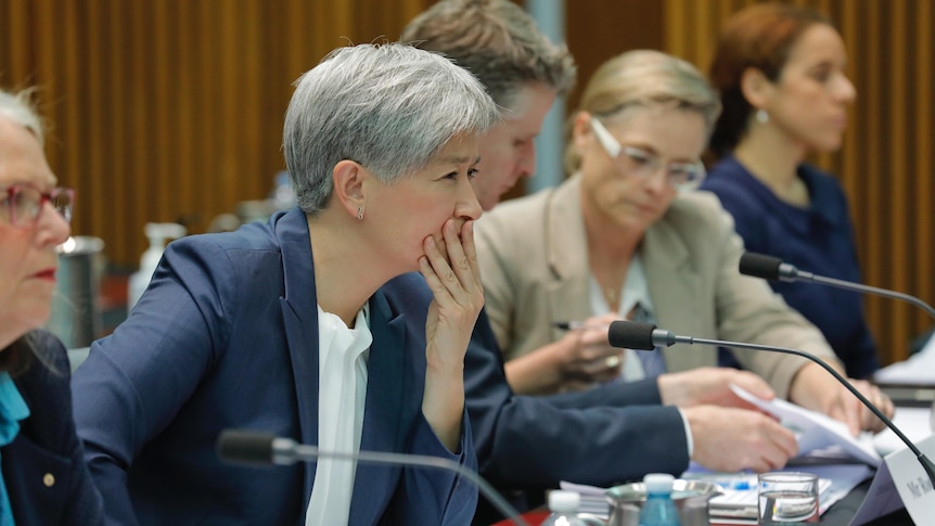 Penny Wong holding her hand up to her mouth pensively during a senate hearing. 