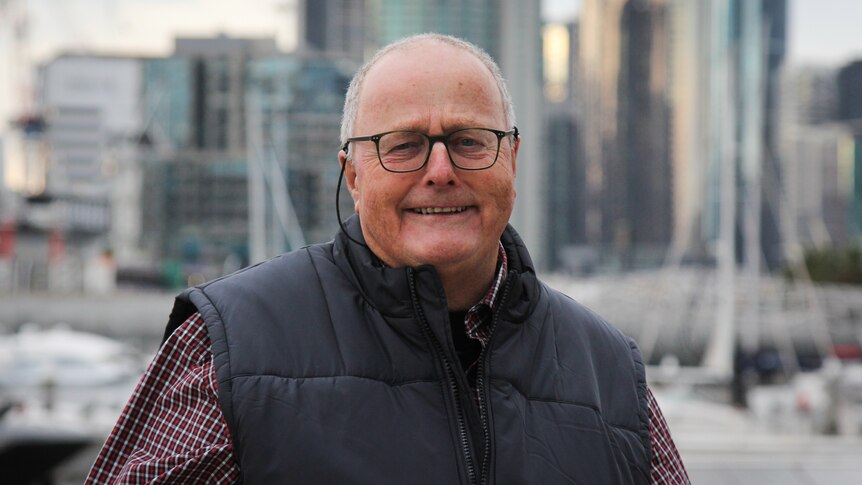 An older man smiling at the camera standing in front of the Melbourne skyline