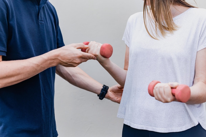 A man helps a woman use light hand weights.