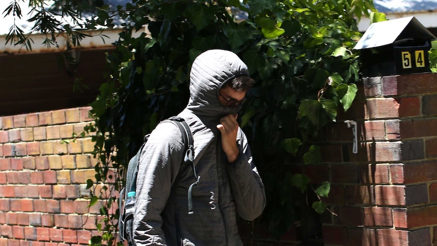 A man wearing a hoodie and with his face obscured walks past a house.