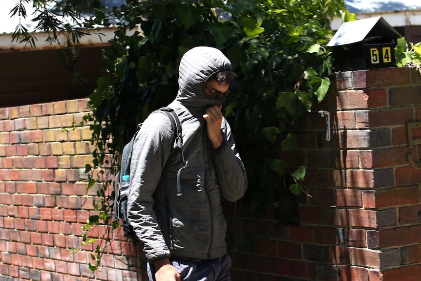 A man wearing a hoodie and with his face obscured walks past a house.