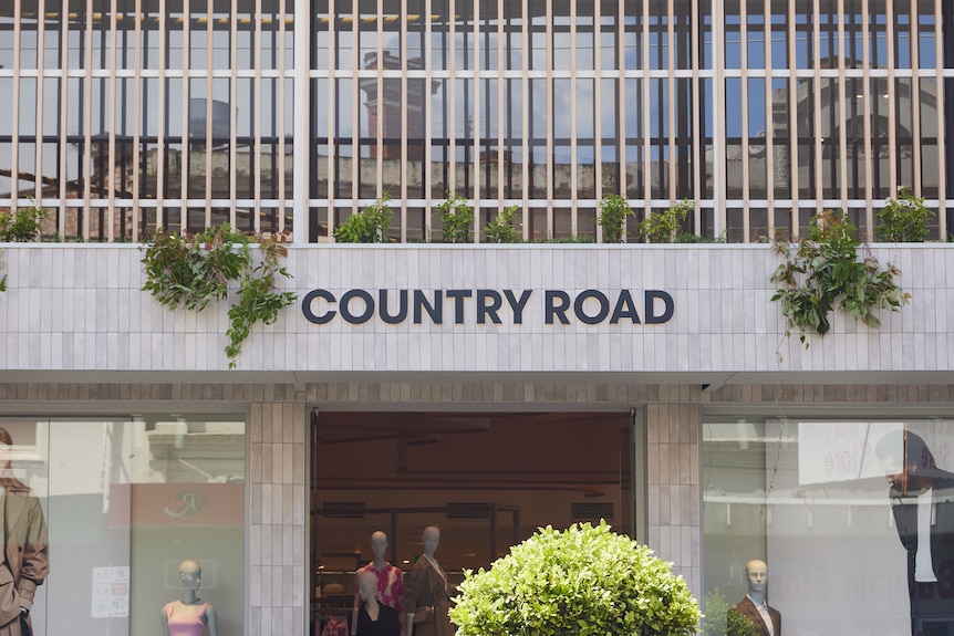 A country road store with a concrete facade, with dummies in the window wearing clothes.