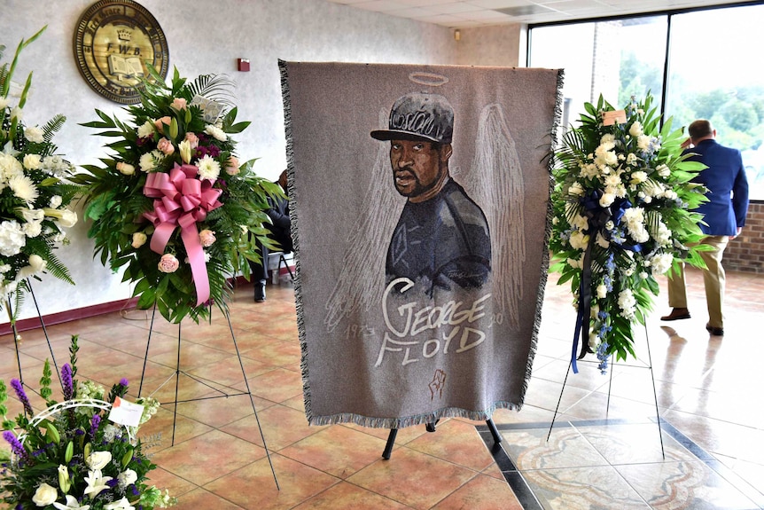 a large hand-drawn image of George Floyd sits upright on a stand among flowers