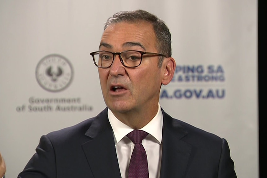Steven Marshall stands in a suit in front of a SA Health and SA Government logo background