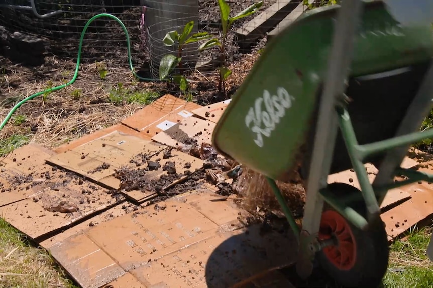 A person tips garden material from a wheelbarrow onto a layer of cardboard.